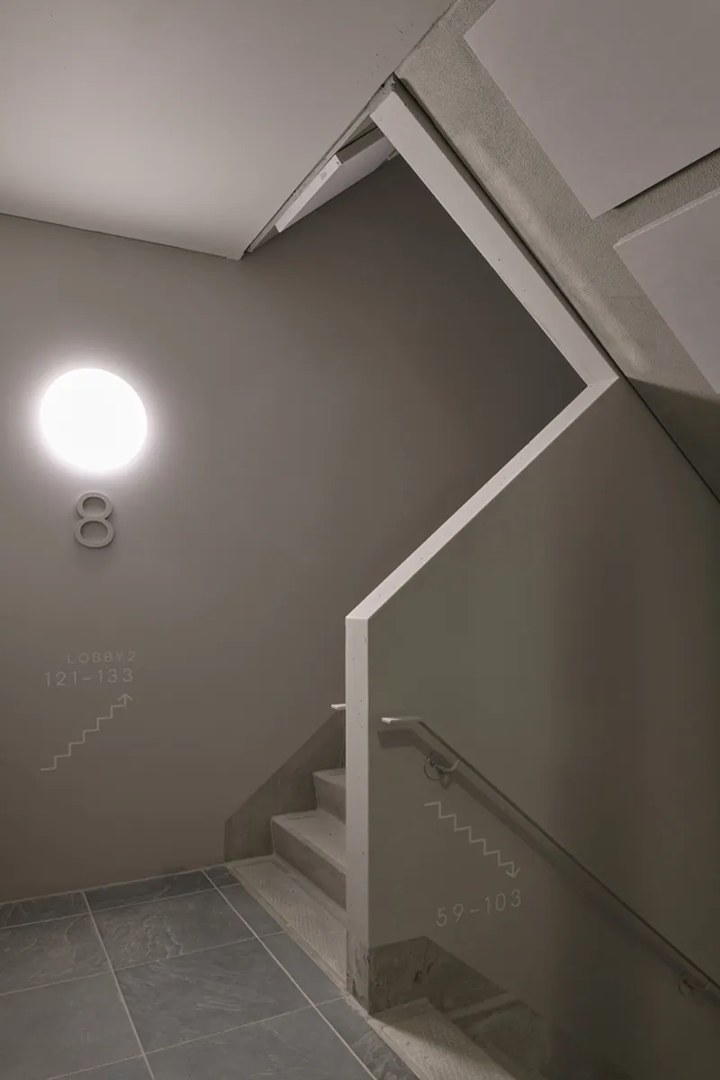 Angular staircase landing with grey walls and circular wall sconce illuminating the corridor