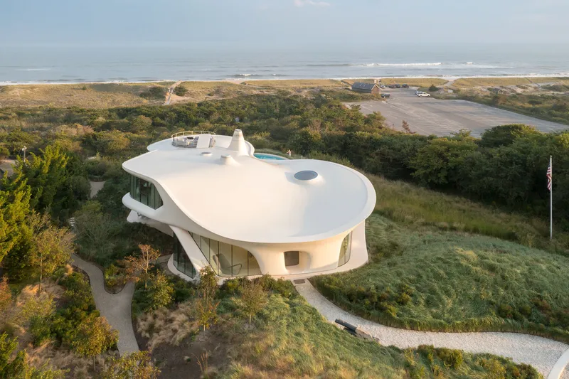 Aerial view of the white curved roof with circular skylights nestled among coastal dunes and vegetation