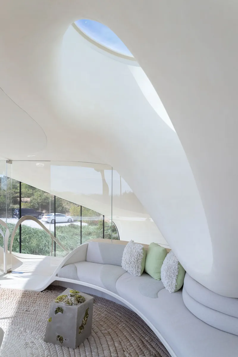 Interior living space with curved white walls and a teardrop-shaped skylight washing light across the ceiling