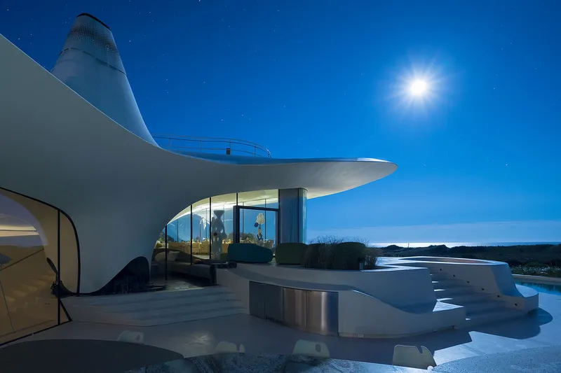 Rooftop terrace with perforated chimney element and curved glass walls illuminated at twilight under moonlight