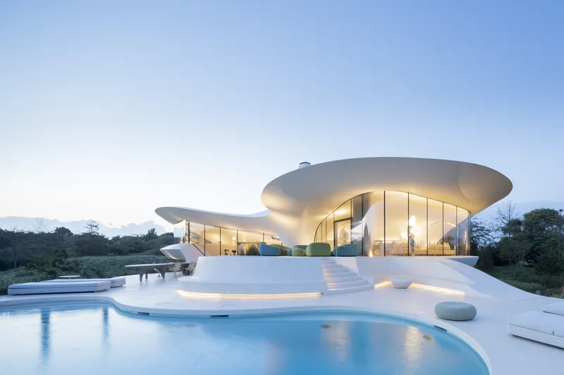 Exterior view at dusk showing the layered cantilevered roof planes and terrace pool glowing with interior light