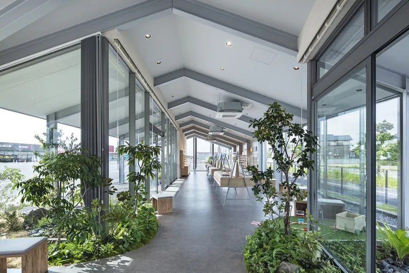 Long interior hallway with rhythmic ceiling beams, glass partitions, and interior plantings on both sides