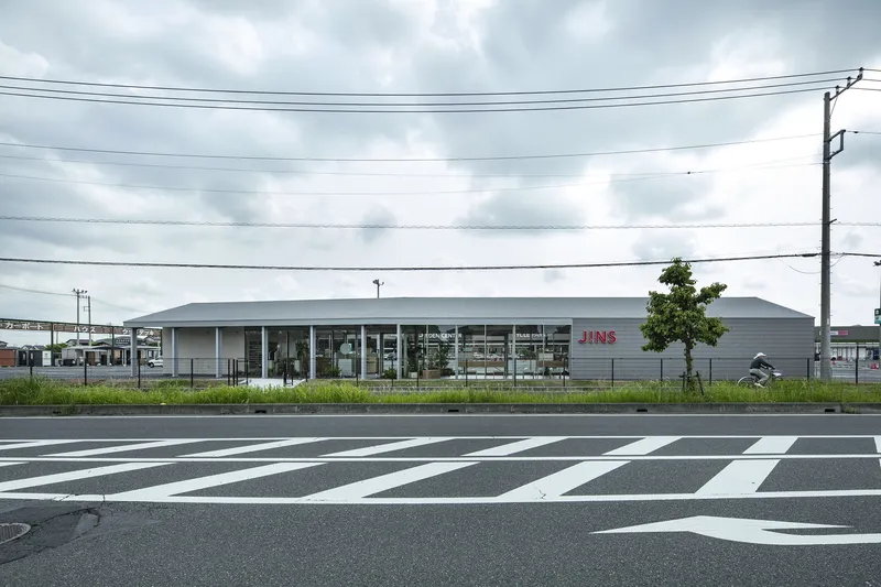Street view of the low horizontal volume with glazed facade and striped pedestrian crossing in foreground