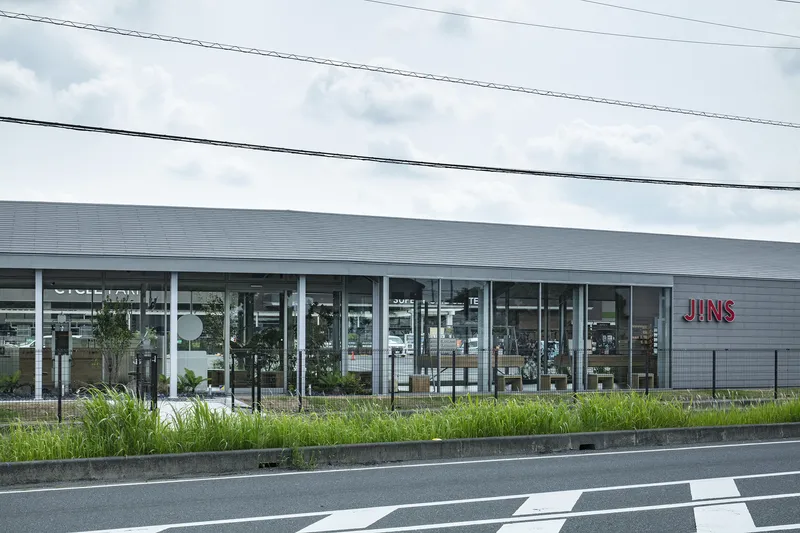 Glazed facade with slender white columns and planted bed along the roadside under overcast sky