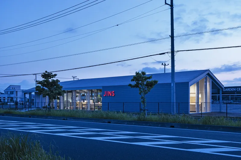 Blue metal-clad retail building with glazed storefront viewed from across the road at dusk