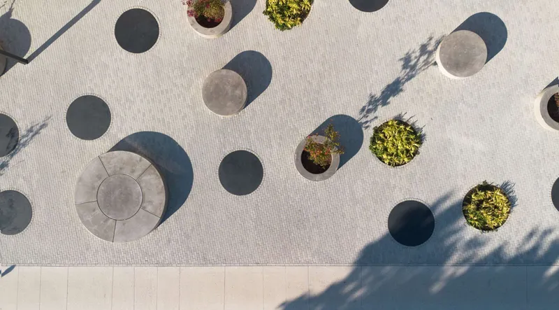 Aerial view of circular concrete planters and tree shadows cast across pale paving
