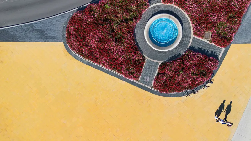 Circular fountain with blue basin surrounded by red groundcover and yellow paving surface