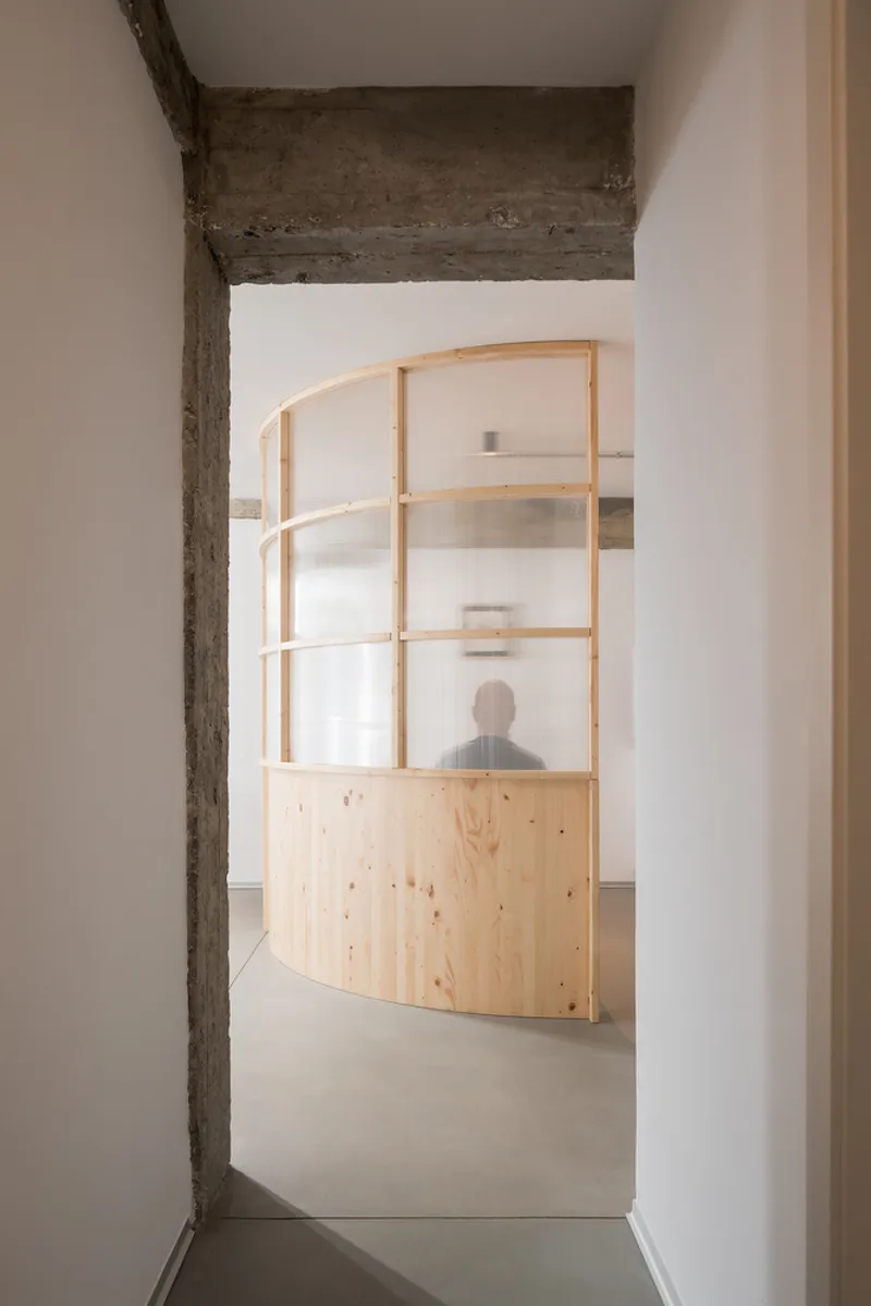 View through an exposed concrete doorway to a curved timber and glass partition with a silhouetted figure