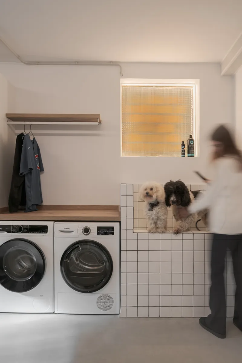 Laundry room with white tile dog bath and backlit glass block window as figure passes