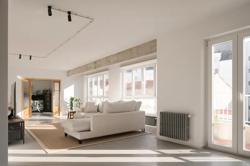 Living room with exposed concrete beam and daylight flooding across polished concrete floor through multiple windows