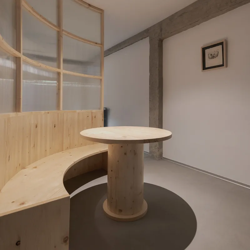 Cylindrical timber table and curved bench beside translucent partition screen in corner beneath concrete beam