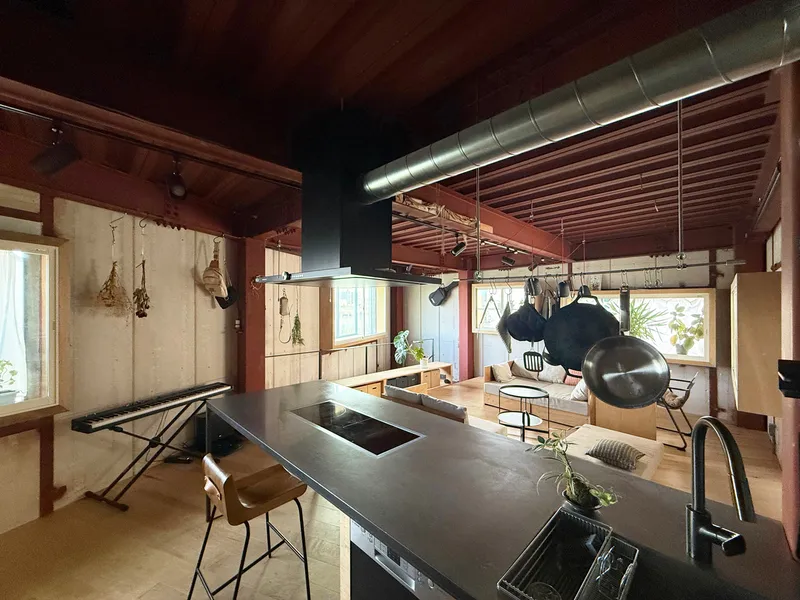 Central island with black countertop and overhead ventilation hood surrounded by timber-clad walls and ceiling