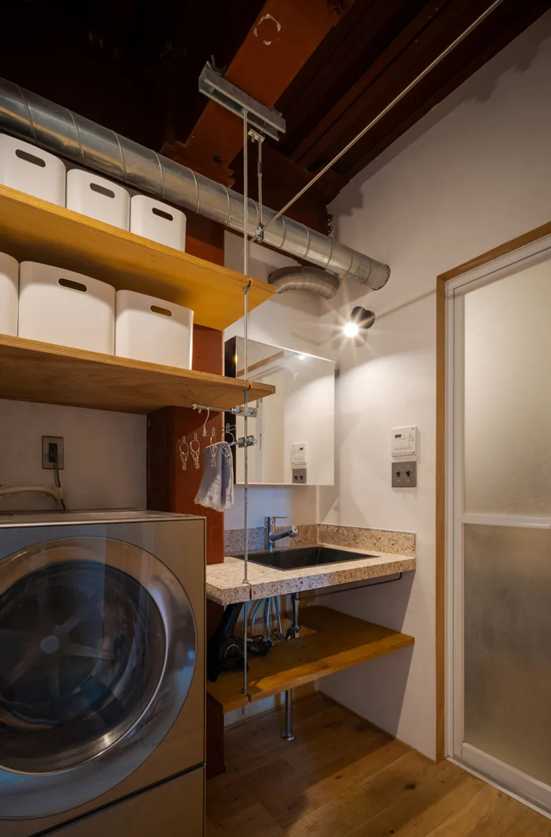 Compact utility room with front-loading washer, terrazzo sink and timber shelving with storage boxes above