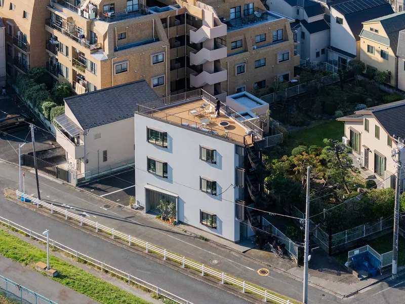 Aerial view of a white three-story building with rooftop deck nestled among surrounding apartment blocks
