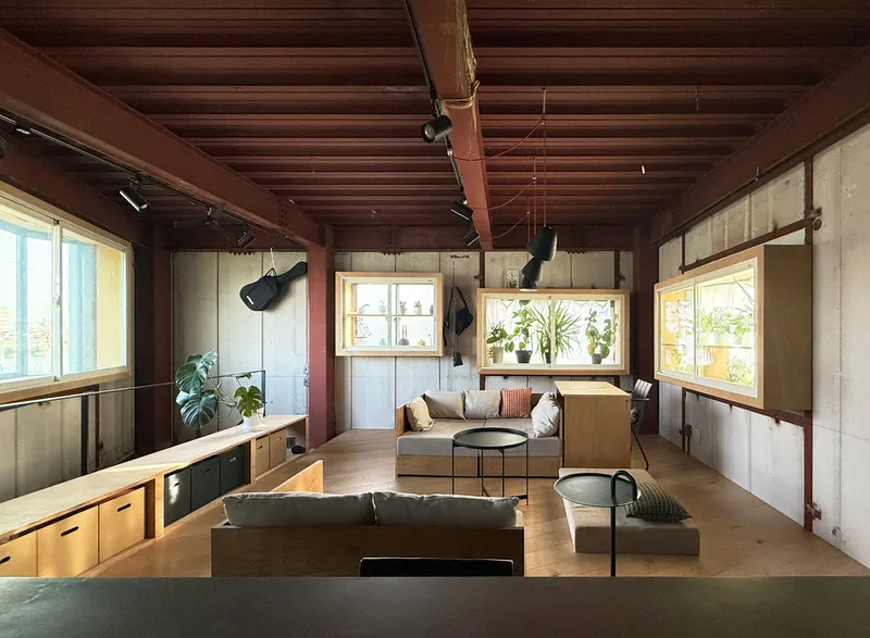 Open living space with exposed timber frame and concrete walls surrounding built-in seating and shelving