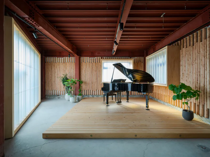 Timber platform with grand piano beneath exposed wood beam ceiling and translucent corrugated wall panels