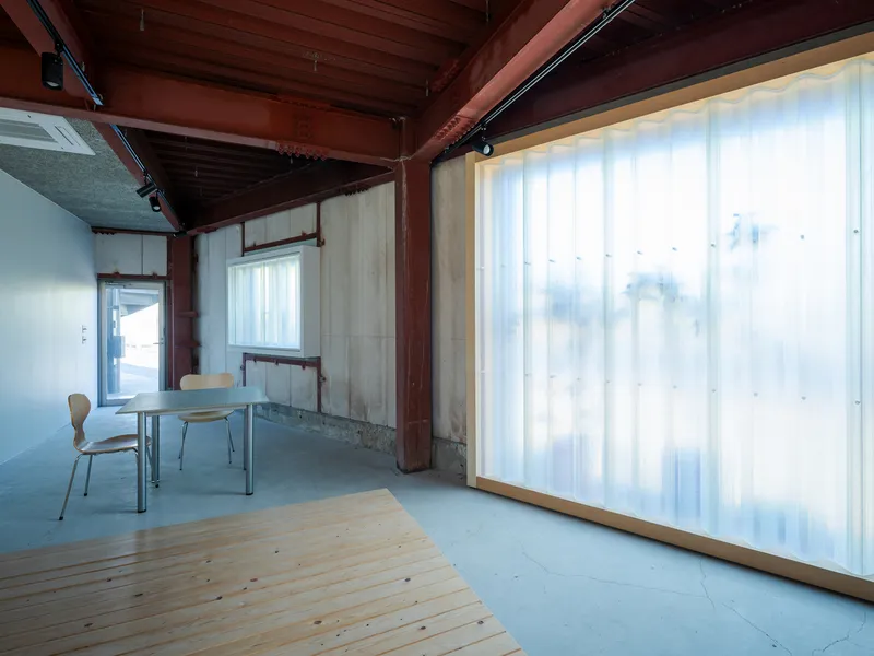 Interior showing concrete floor meeting timber deck with translucent corrugated panels filtering daylight