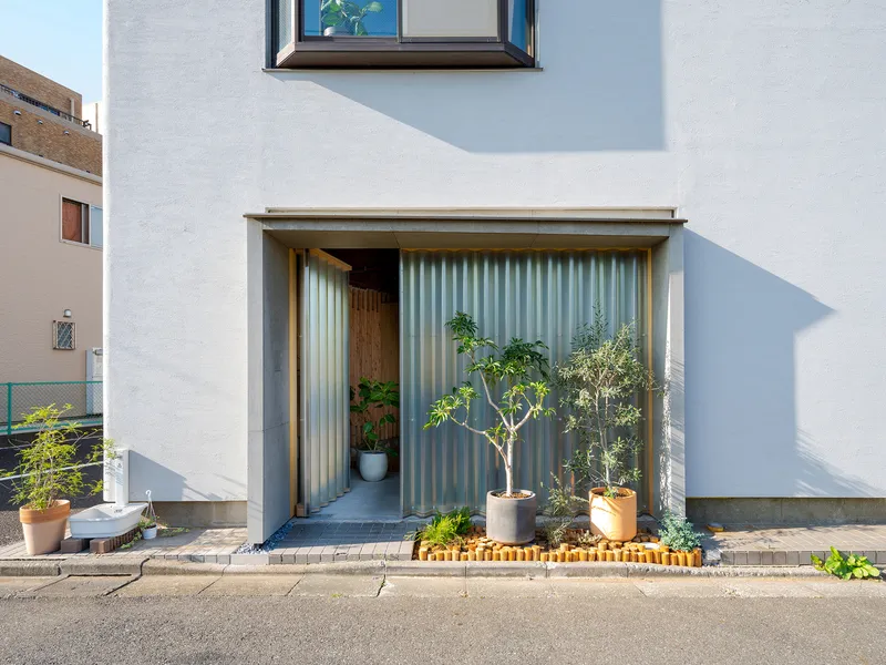Street-facing entrance with corrugated metal surround and potted plants in afternoon sun