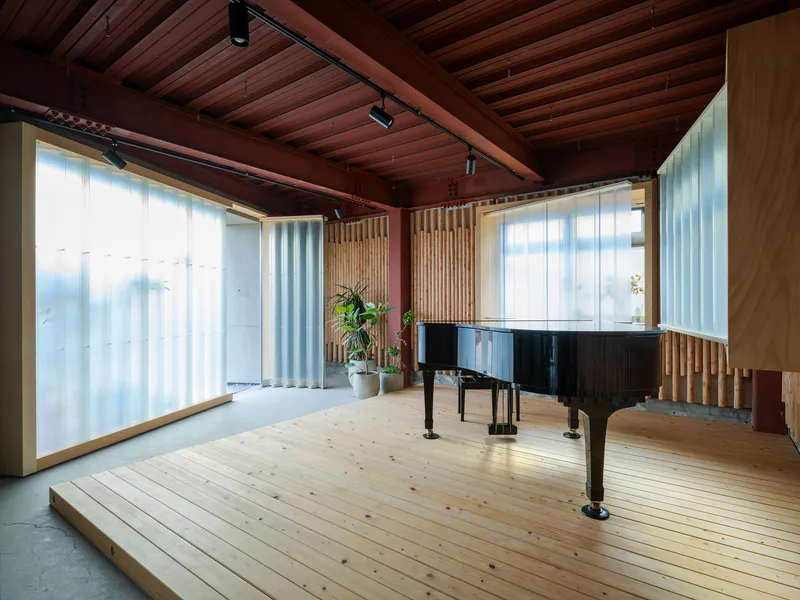 Corner view of timber platform with grand piano beneath translucent corrugated panels and exposed ceiling beams