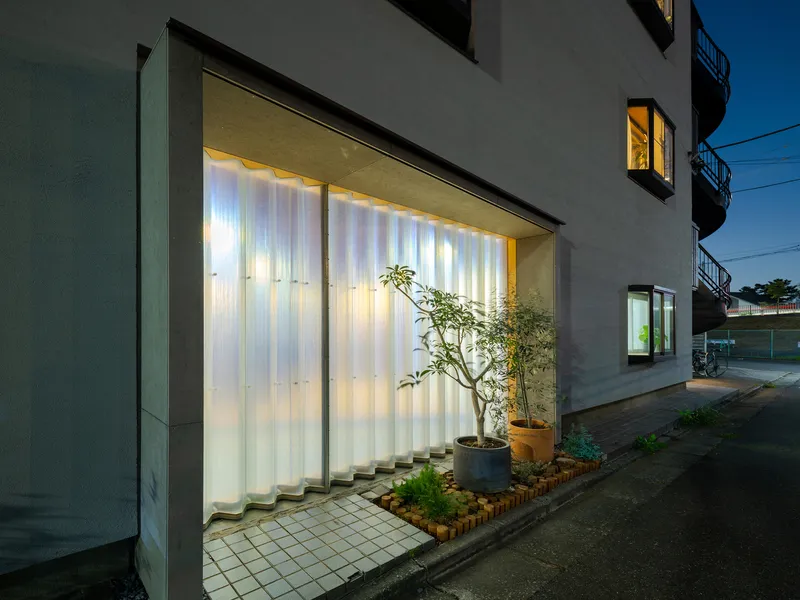 Street facade with illuminated translucent wall panels and potted trees at dusk