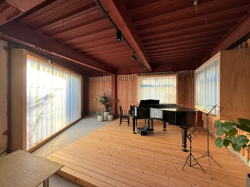 Music room with exposed timber ceiling, corrugated metal wall panels, and translucent curtains filtering daylight
