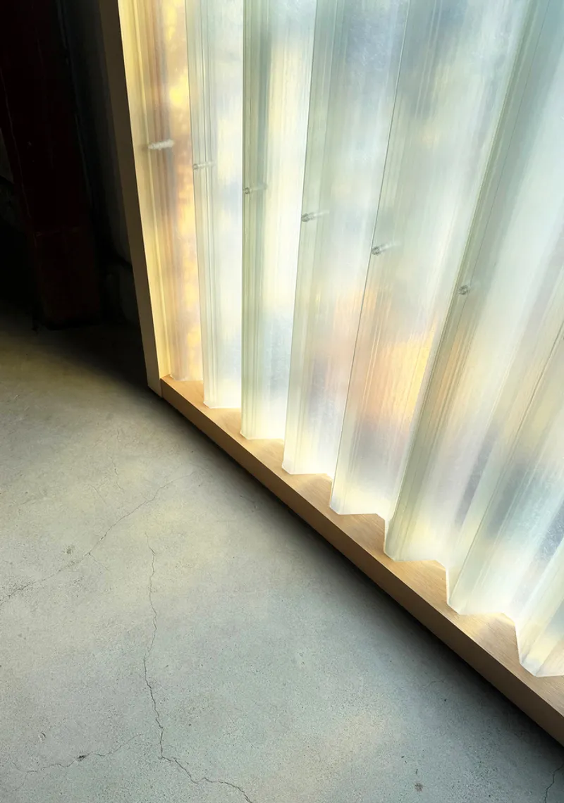Close-up of backlit translucent panel wall with timber trim meeting concrete floor