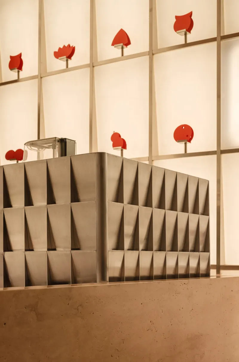 Angled timber display slots with red objects suspended on backlit wall grid behind terrazzo floor
