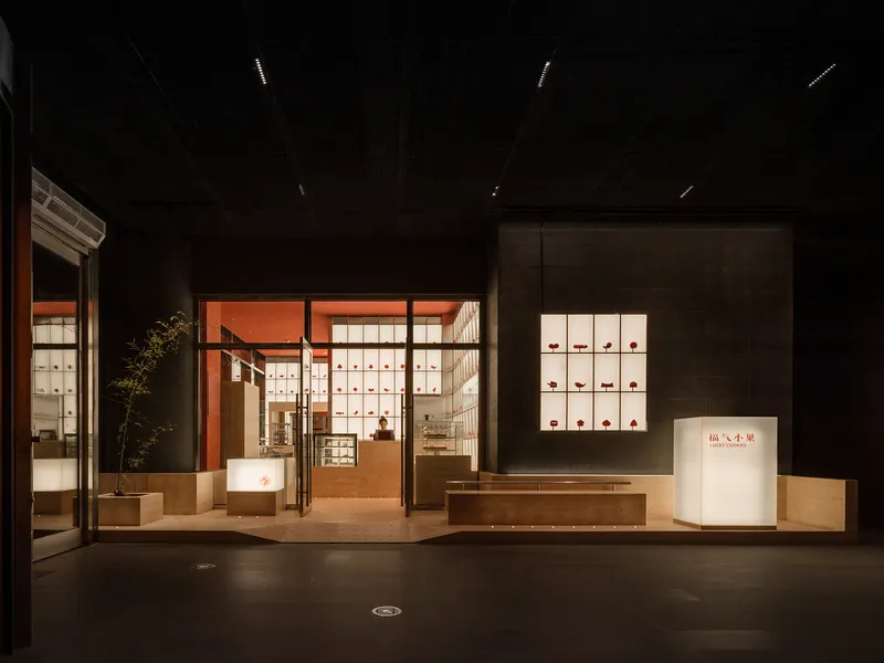 Storefront facade with illuminated display volumes in orange and glass within a dark interior space