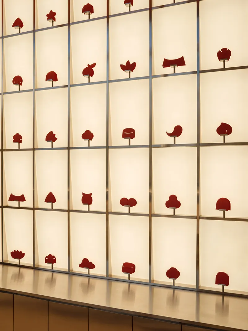 Backlit display wall with gridded translucent panels featuring red tree-shaped objects in each compartment
