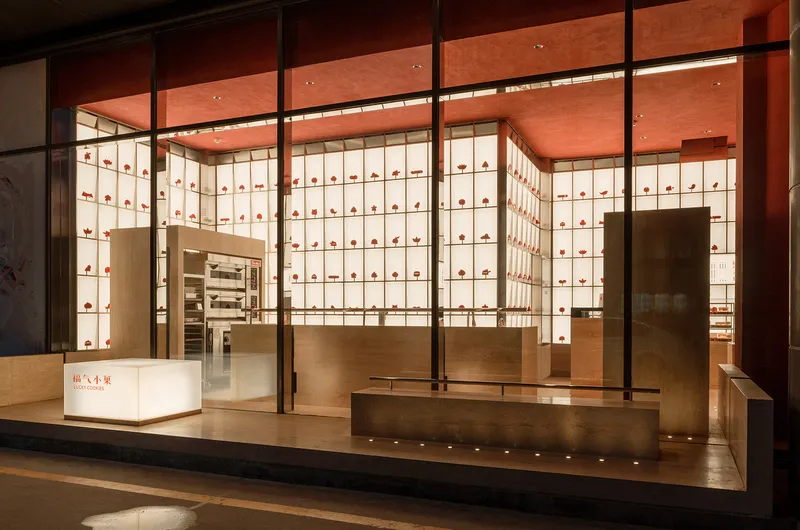 Storefront view through glass showing illuminated display wall and timber counter beneath a red ceiling