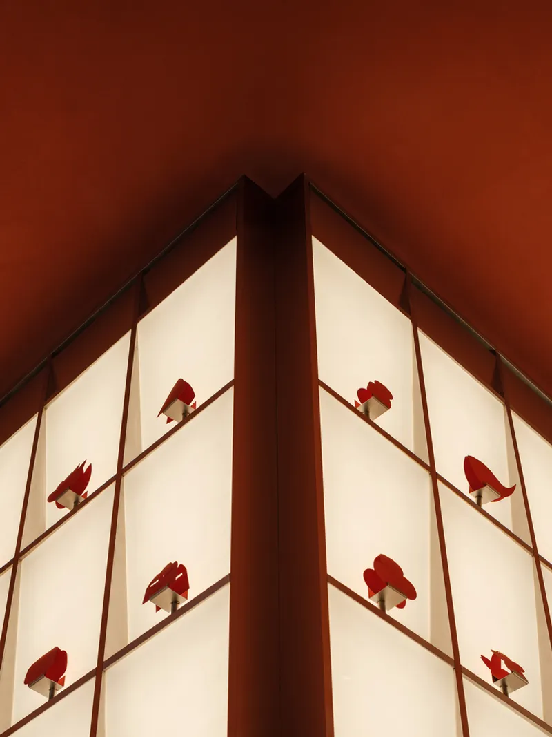 Corner view of illuminated translucent wall panels with red silhouette ornaments framed by dark timber mullions
