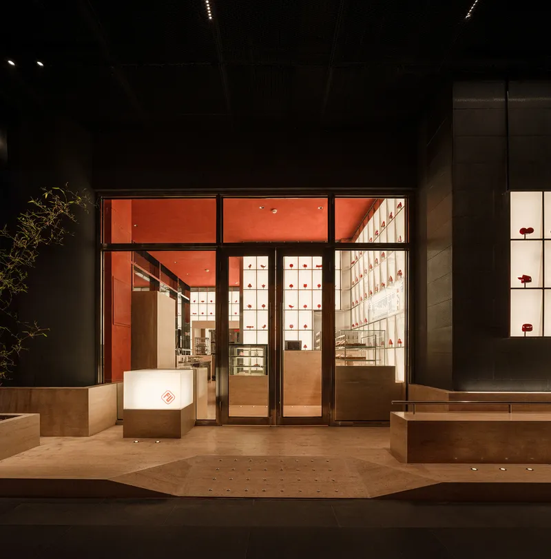 Entrance at dusk with glazed doors opening to illuminated interior and a bare tree beside the entry