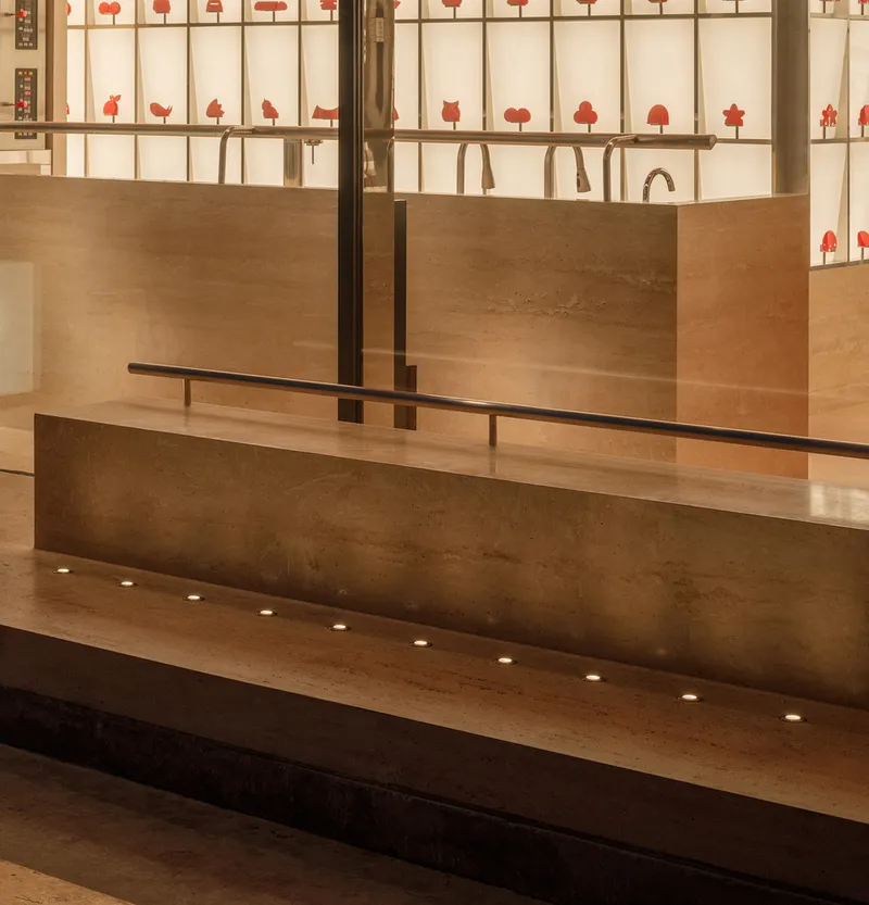 Detail of timber service counter with bronze faucets and recessed floor lighting beneath stepped platform