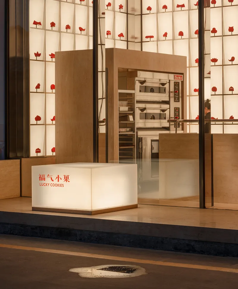 Storefront threshold showing timber platform, gridded display wall with red objects, and illuminated signage cube