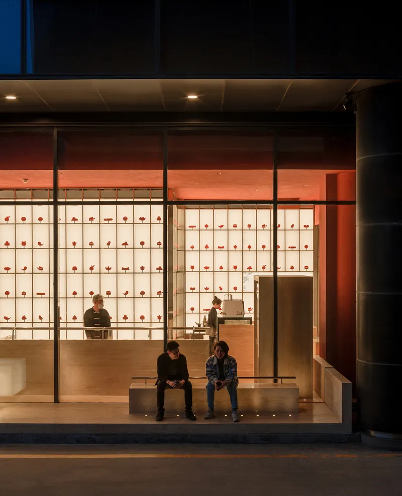 Street view of glazed shopfront at dusk with seated customers on timber bench inside