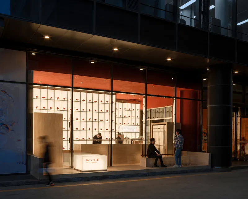 Shopfront entrance at twilight with pedestrians passing and an illuminated product display grid inside