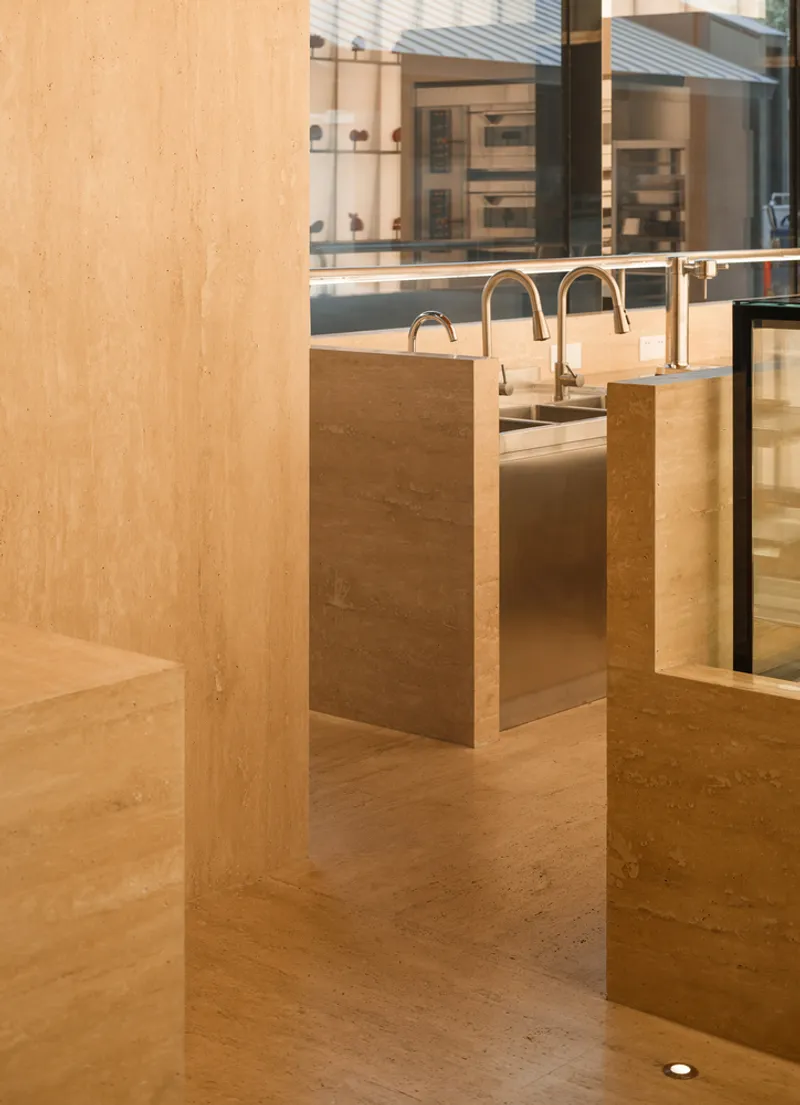 Timber column and rammed earth counter with brass tap fixtures in afternoon sunlight