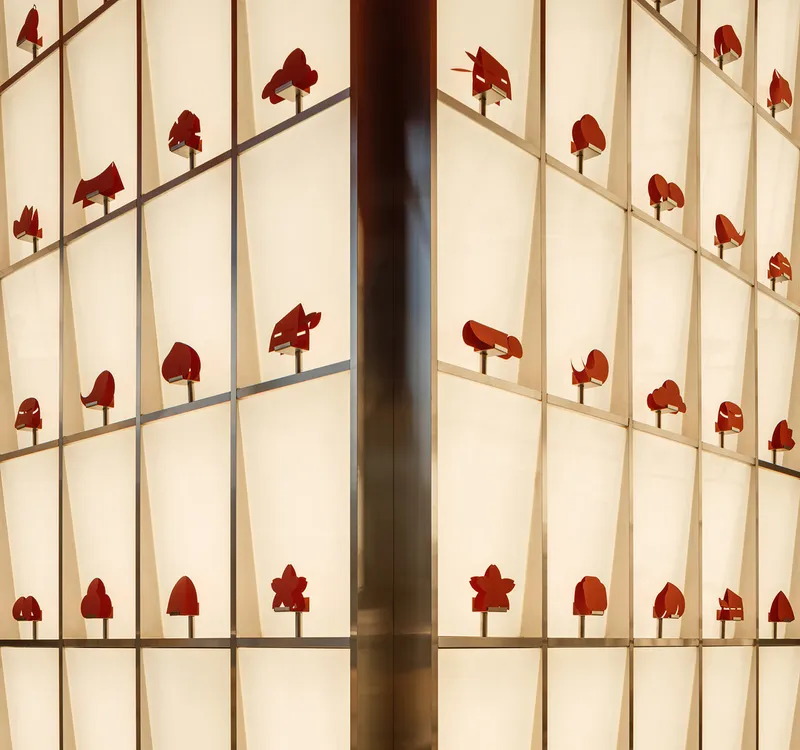 Backlit translucent wall grid with red wooden tree silhouettes casting shadows across the panels