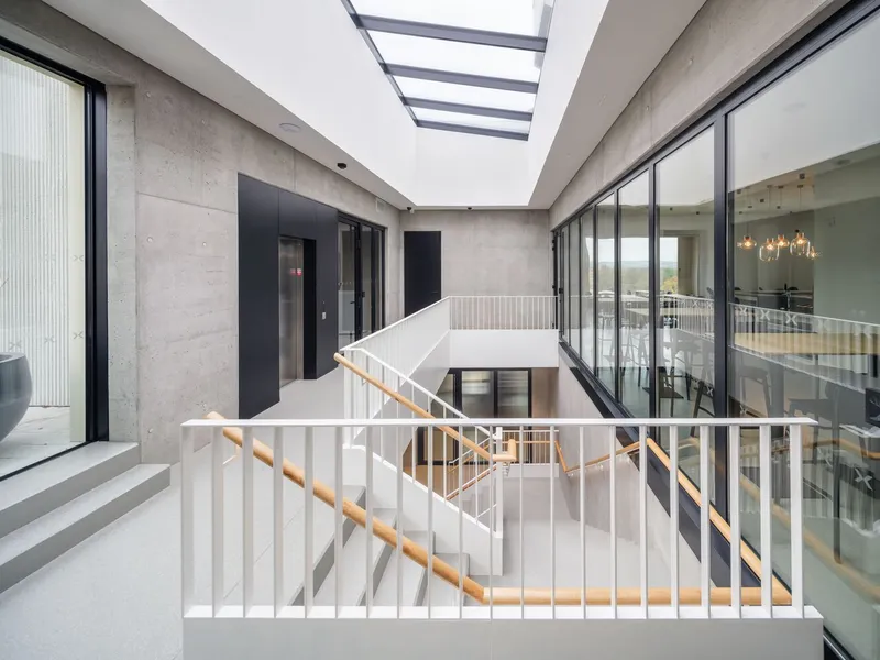 Interior stairwell with white metal railings and timber handrail beneath a slatted skylight