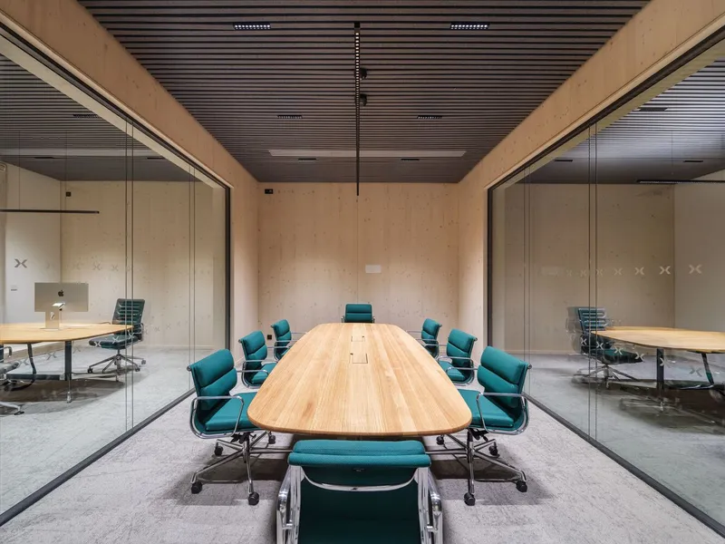 Conference room with plywood walls and slatted ceiling flanked by glass partitions to adjacent workspaces