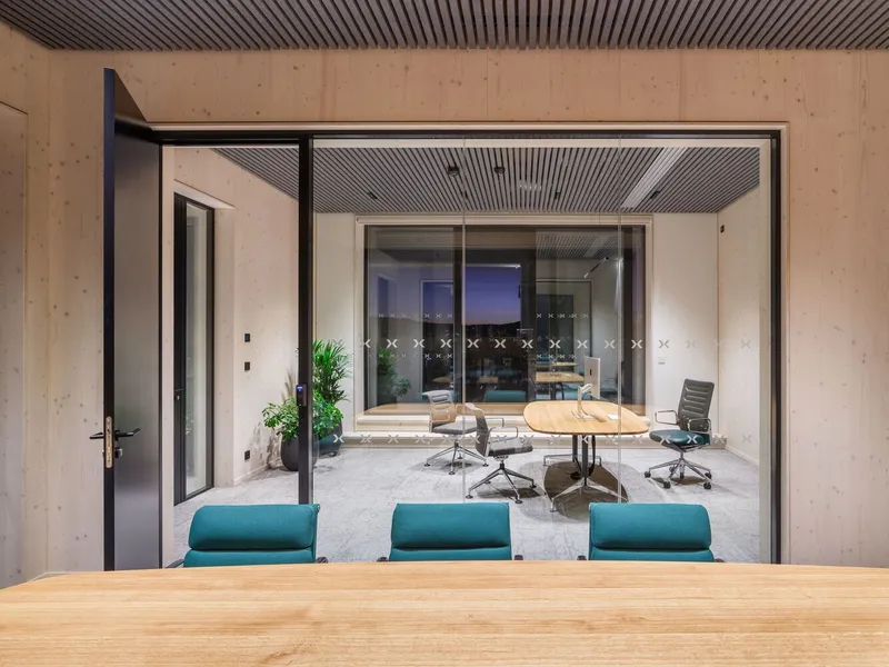 View through glass partitions from one meeting room into another with plywood walls at dusk
