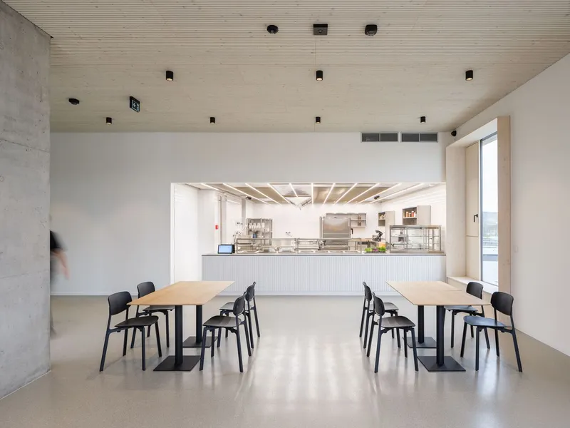 Dining area with two timber tables facing a white service counter framed by exposed ceiling joists