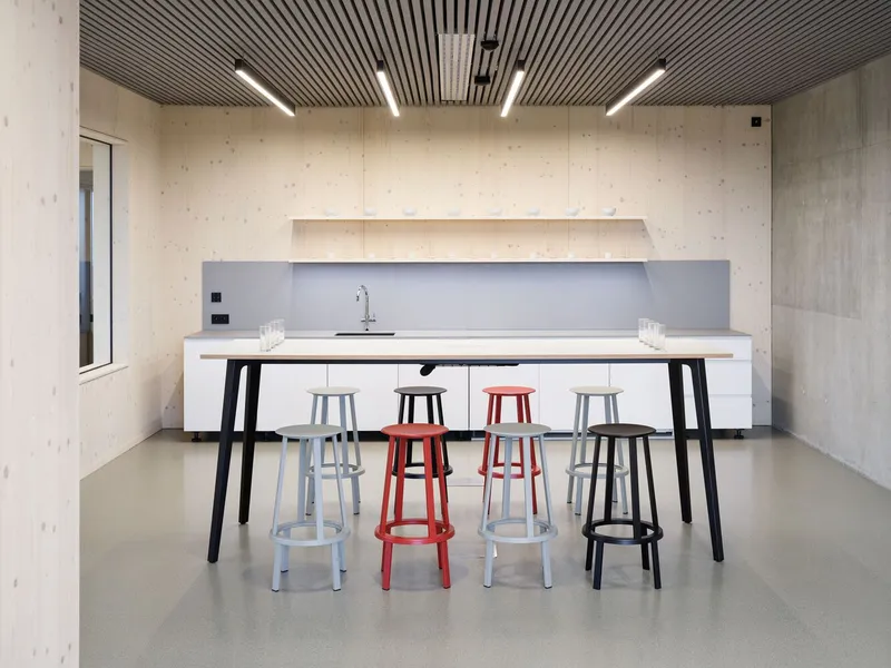 Workspace with white high table surrounded by colorful stools beneath a slatted timber ceiling