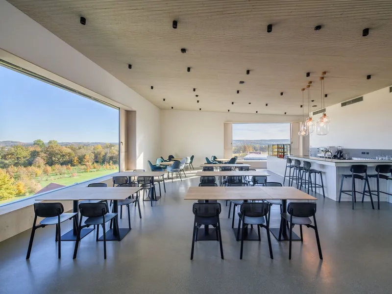 Corner glazing frames autumn foliage beyond rows of dining tables and a bar with pendant lights