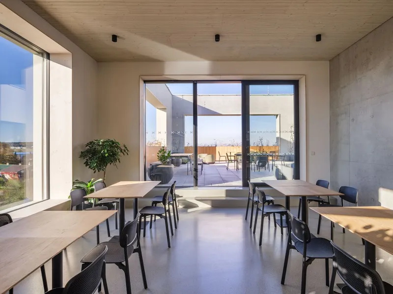 Dining space with timber tables and potted plants facing glass doors opening to an exterior terrace