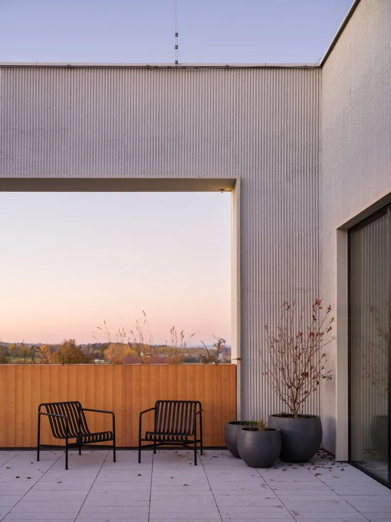 Rooftop terrace with two metal chairs and planted pots framed by corrugated metal walls at dusk