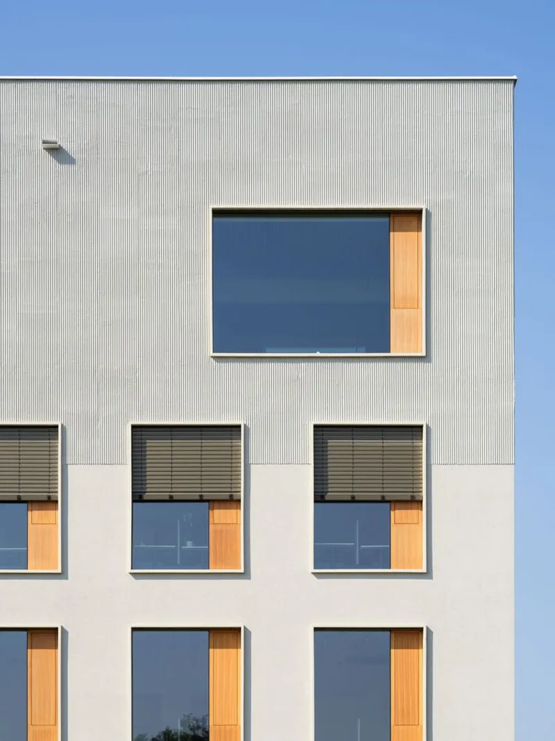 Facade detail showing corrugated metal cladding above smooth render with timber-lined window openings and exterior blinds