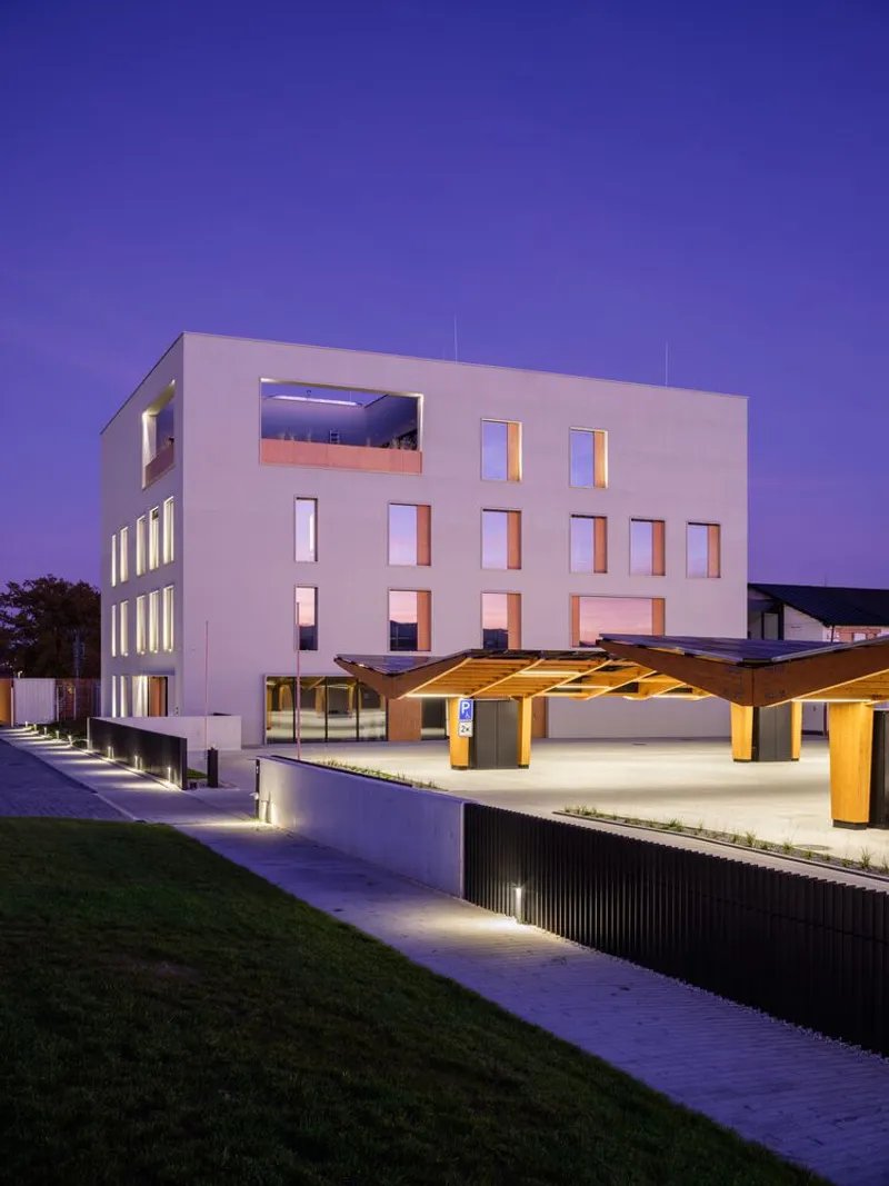 Timber pergola canopy with illuminated columns beside the building at twilight