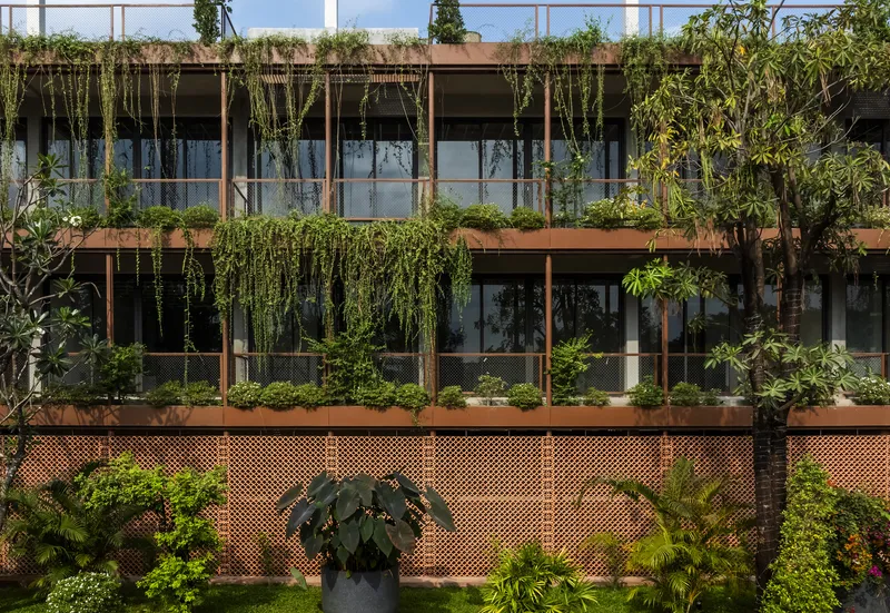 Facade detail showing timber frames with hanging plants above a perforated brick base wall