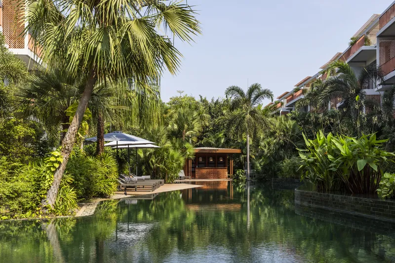 Poolside pavilion with timber screens surrounded by palm trees and tropical planting